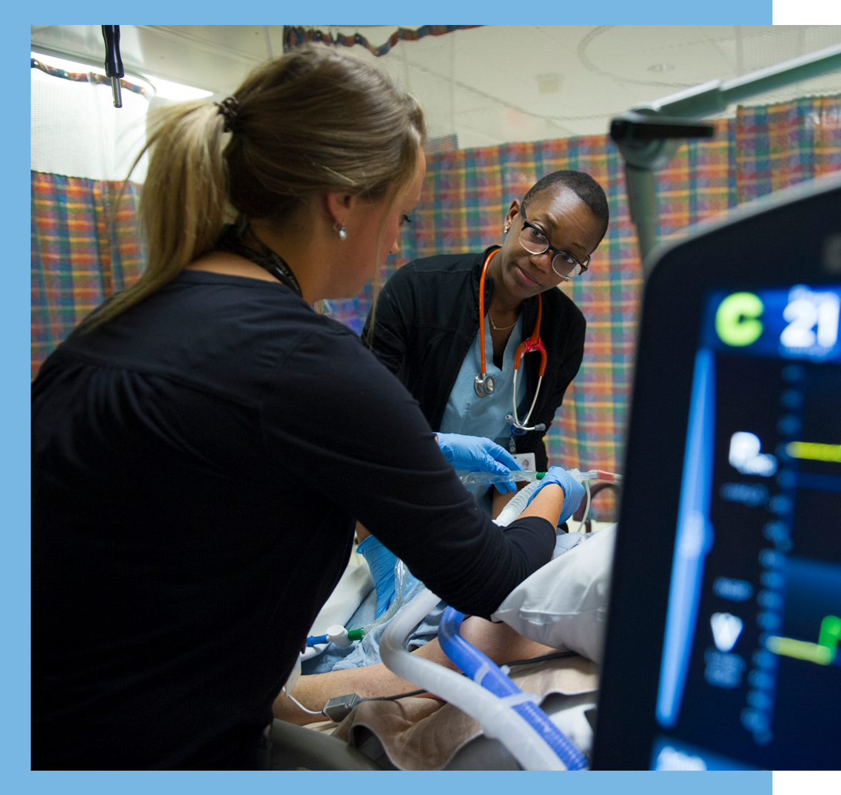 Health-care worker looks at their colleague as they both care for a patient.